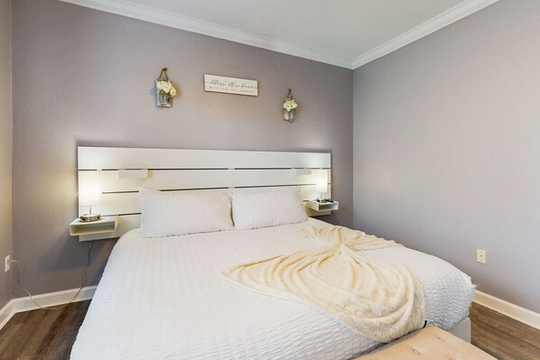 A neatly made bed with a white headboard, two bedside lamps, and a wall-mounted sign. - Tuscana Resort | 2BR/2BA Kissimmee Condo with Communal Pool (Kissimmee)