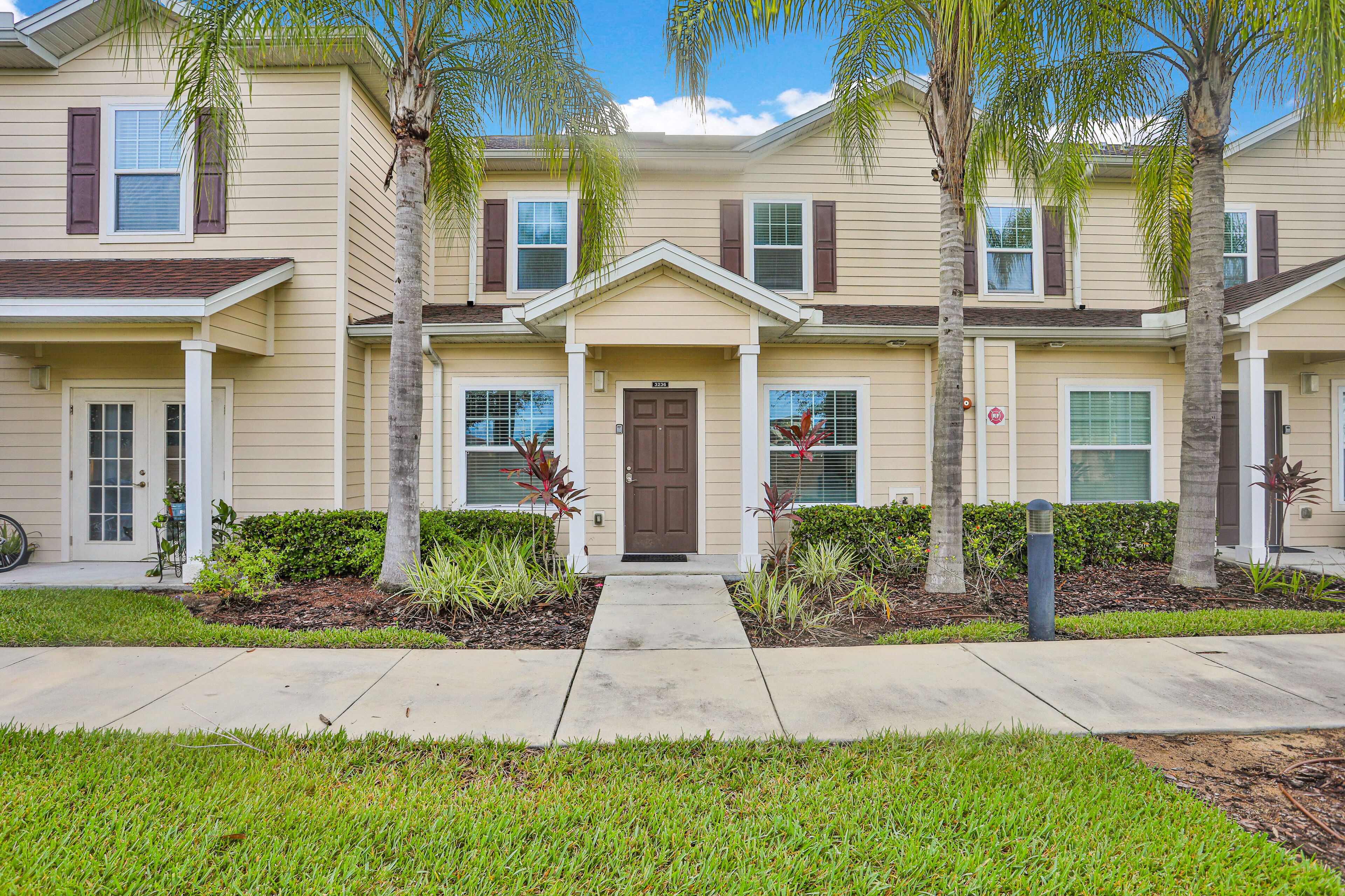 A multi-story residential building with a central entrance, surrounded by well-maintained landscaping and palm trees.
