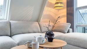Uma sala de estar moderna com um sofá cinza, uma mesa de centro de madeira e um vaso com galhos.