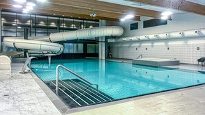 Piscina interna com escorrega, paredes azulejadas e teto de madeira.