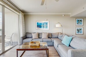 A modern living room with a grey sectional sofa, a glass coffee table, and a large window with curtains. - Unwind in a lakefront condo with AC, pool, hot tub & fitness center close to fun (Orlando)