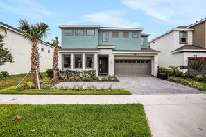 A two-story house with a garage, a well-maintained lawn, and palm trees. - Dog-friendly home with a heated pool, pool spa, in-home theater, lanai, & patio (Kissimmee)