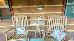 Two wooden chairs with floral cushions, a small table with a candle, and a wall-mounted decoration. - Log Cabin Mountain Retreat,  2-bedroom cabin in Mills River North Carolina (Horse Shoe)