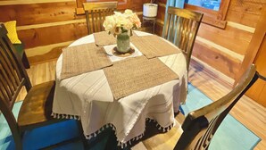 A wooden cabin interior with a round dining table covered with a white tablecloth, surrounded by wooden chairs. - Log Cabin Mountain Retreat,  2-bedroom cabin in Mills River North Carolina (Horse Shoe)