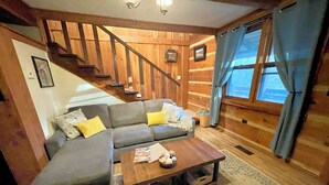 A cozy living room with a sectional sofa, a coffee table, and a staircase leading to an upper level. - Log Cabin Mountain Retreat,  2-bedroom cabin in Mills River North Carolina (Horse Shoe)