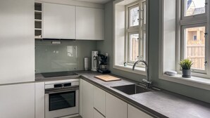 A modern kitchen with white cabinets, a built-in oven, a coffee maker, and a window with a view of a wooden fence. - 2 bedroom stunning home in Haugesund (Haugesund)