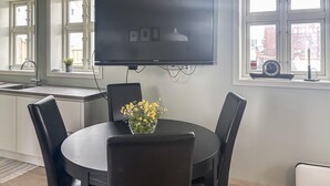 A modern kitchen with a dining area, featuring a large flat-screen TV mounted above a dark wooden table surrounded by chairs, a vase of yellow flowers, and a view of the city through large windows. - 2 bedroom stunning home in Haugesund (Haugesund)