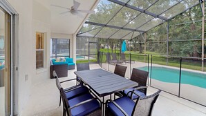Eine überdachte Terrasse mit Tisch und Stühlen, einem Deckenventilator und Blick auf einen Swimmingpool.