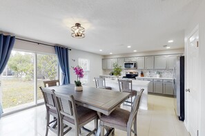 A modern kitchen with white cabinets, a central island, and a dining area with a wooden table and chairs. - 5BR Kissimmee Retreat w/ Private Pool & Game Room (Kissimmee)