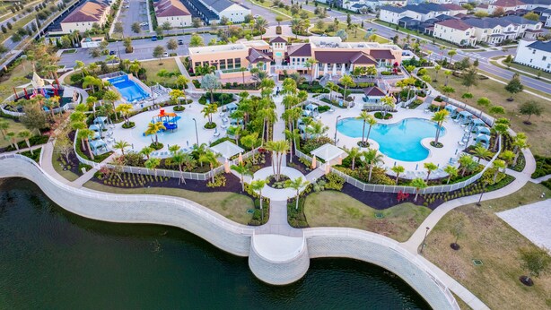 Vista aérea de una zona residencial con piscina central, un puente sobre el agua y casas aledañas.