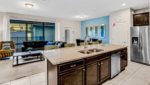A modern kitchen with a central island, stainless steel appliances, and a dining area with a sofa and chairs. - Updated & colorful home w/ a modern kitchen, furnished lanai, & private pool (Kissimmee)