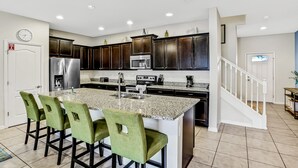 A modern kitchen with granite countertops, dark wooden cabinets, and a central island with bar stools. - Updated & colorful home w/ a modern kitchen, furnished lanai, & private pool (Kissimmee)