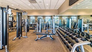 A gym with various exercise equipment, including weight machines and free weights, arranged in a spacious layout with large windows allowing natural light. - Updated & colorful home w/ a modern kitchen, furnished lanai, & private pool (Kissimmee)