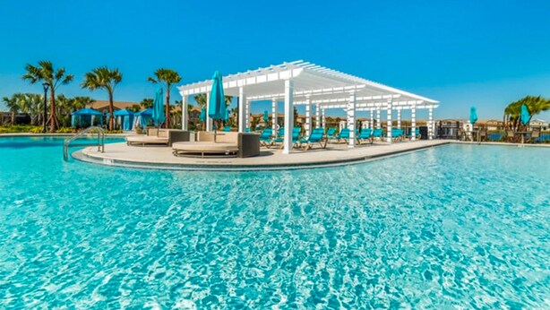 A swimming pool with a white pergola and lounge chairs, surrounded by palm trees and umbrellas. - Updated & colorful home w/ a modern kitchen, furnished lanai, & private pool (Kissimmee)