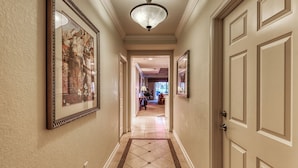 A hallway with framed artwork on the walls, a chandelier, and a door leading to another room. - Family-Friendly Condo with Access to Shared Pools, Hot Tub, and Game Rooms (Kissimmee)