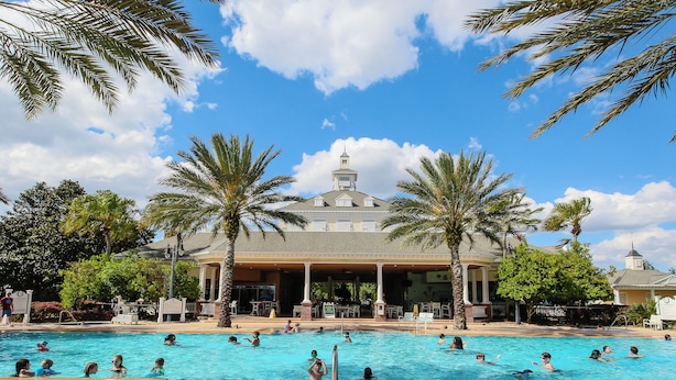 A large outdoor swimming pool with palm trees and a building in the background. - Family-Friendly Condo with Access to Shared Pools, Hot Tub, and Game Rooms (Kissimmee)