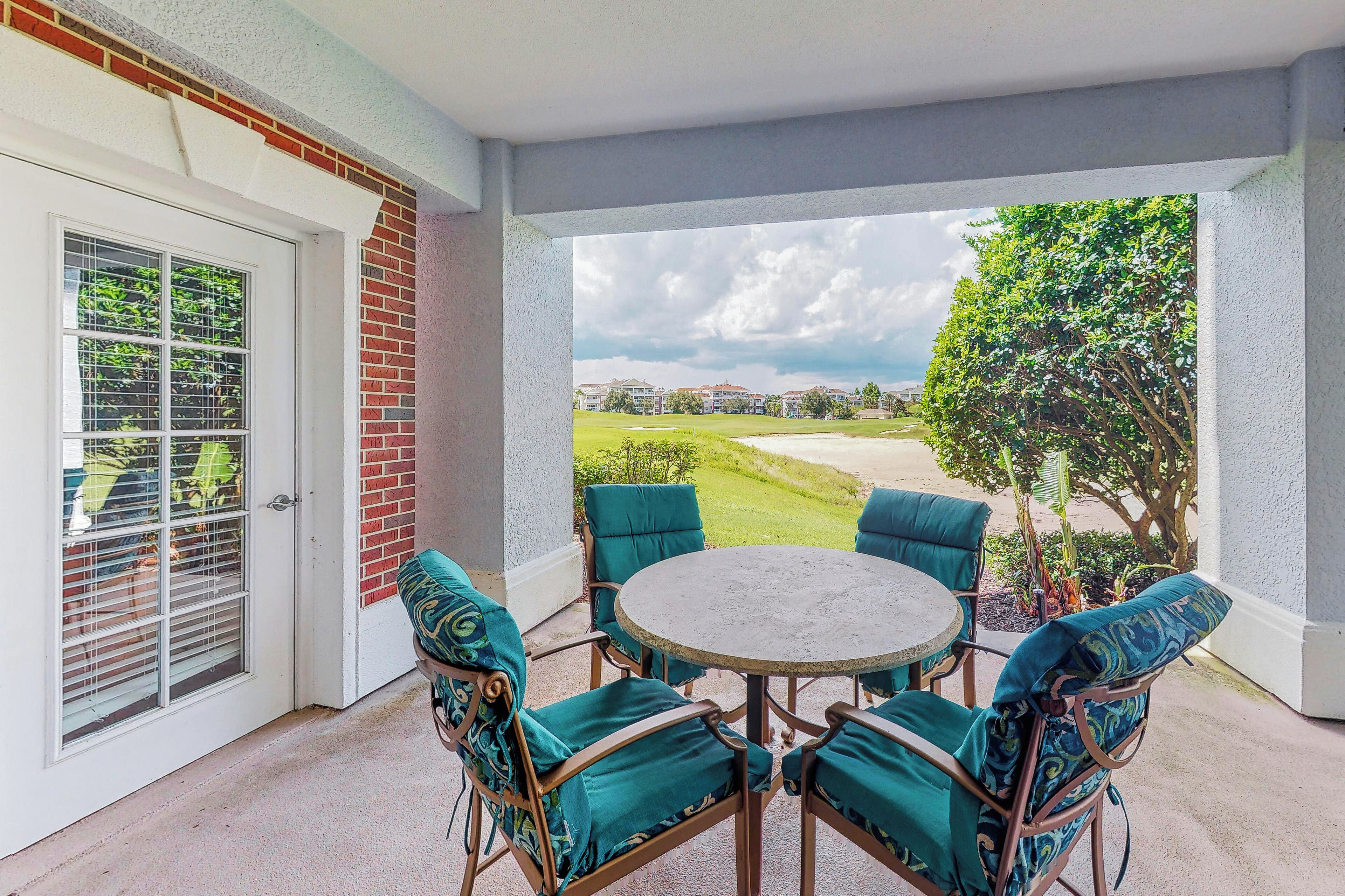 Un patio couvert avec une table ronde et quatre chaises, une porte avec une fenêtre, et une vue sur un terrain de golf.