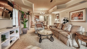 A spacious living room with a ceiling fan, a large window with curtains, a fireplace, and a dining area in the background. - Family-Friendly Condo with Access to Shared Pools, Hot Tub, and Game Rooms (Kissimmee)