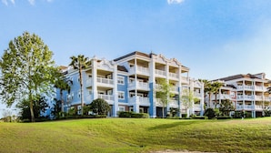A multi-story hotel with balconies, a grassy lawn, and a sandy area. - Family-Friendly Condo with Access to Shared Pools, Hot Tub, and Game Rooms (Kissimmee)