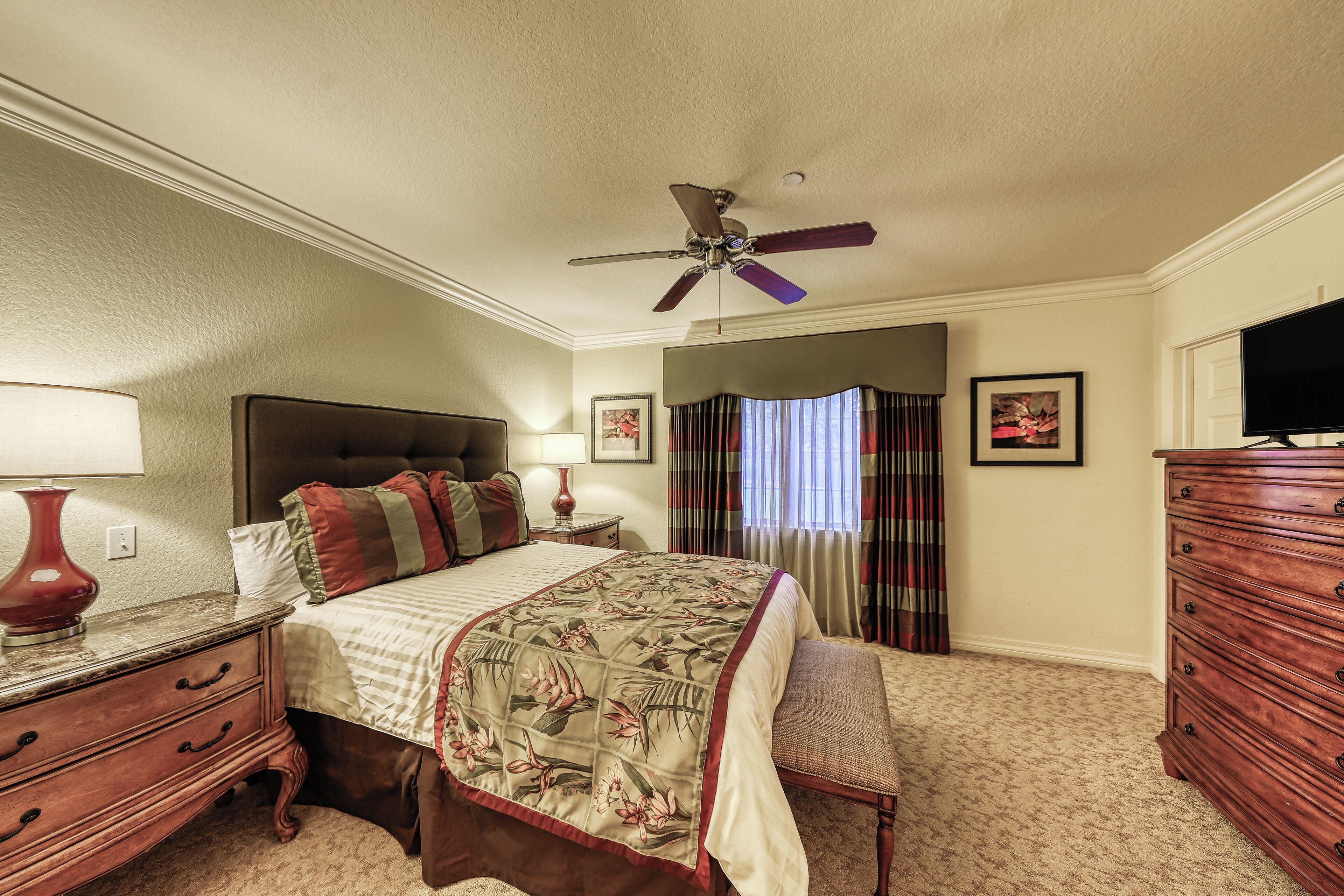 A hotel bedroom with a bed, a dresser, a television, and a ceiling fan.