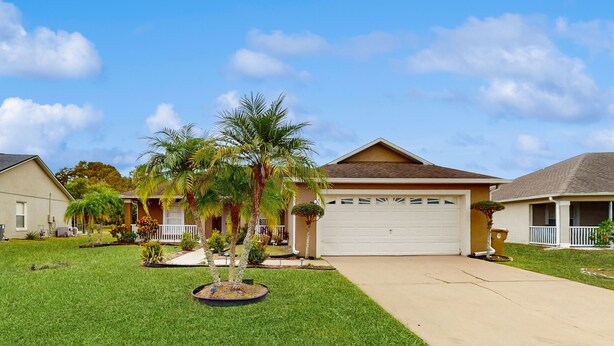 A residential house with a front yard, a garage, and a well-maintained lawn. - Inviting pool home with tranquil pond view near theme parks & attractions (Kissimmee)