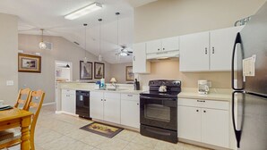 A modern kitchen with white cabinets, a black refrigerator, and a built-in oven. There is a dining table with chairs and a rug on the floor. - Inviting pool home with tranquil pond view near theme parks & attractions (Kissimmee)