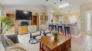 A living room with a sofa, a coffee table, a TV, a wooden cabinet, and a bar area with stools. - Inviting pool home with tranquil pond view near theme parks & attractions (Kissimmee)