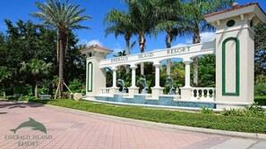 A white entrance archway with 'Emerald Island Resort' written on it, surrounded by palm trees and a water feature. - Spacious 6BR resort home with private pool, game room & near Disney parks (Kissimmee)