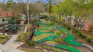 Un campo de golf con múltiples zonas verdes, un área de juegos infantiles y árboles circundantes.