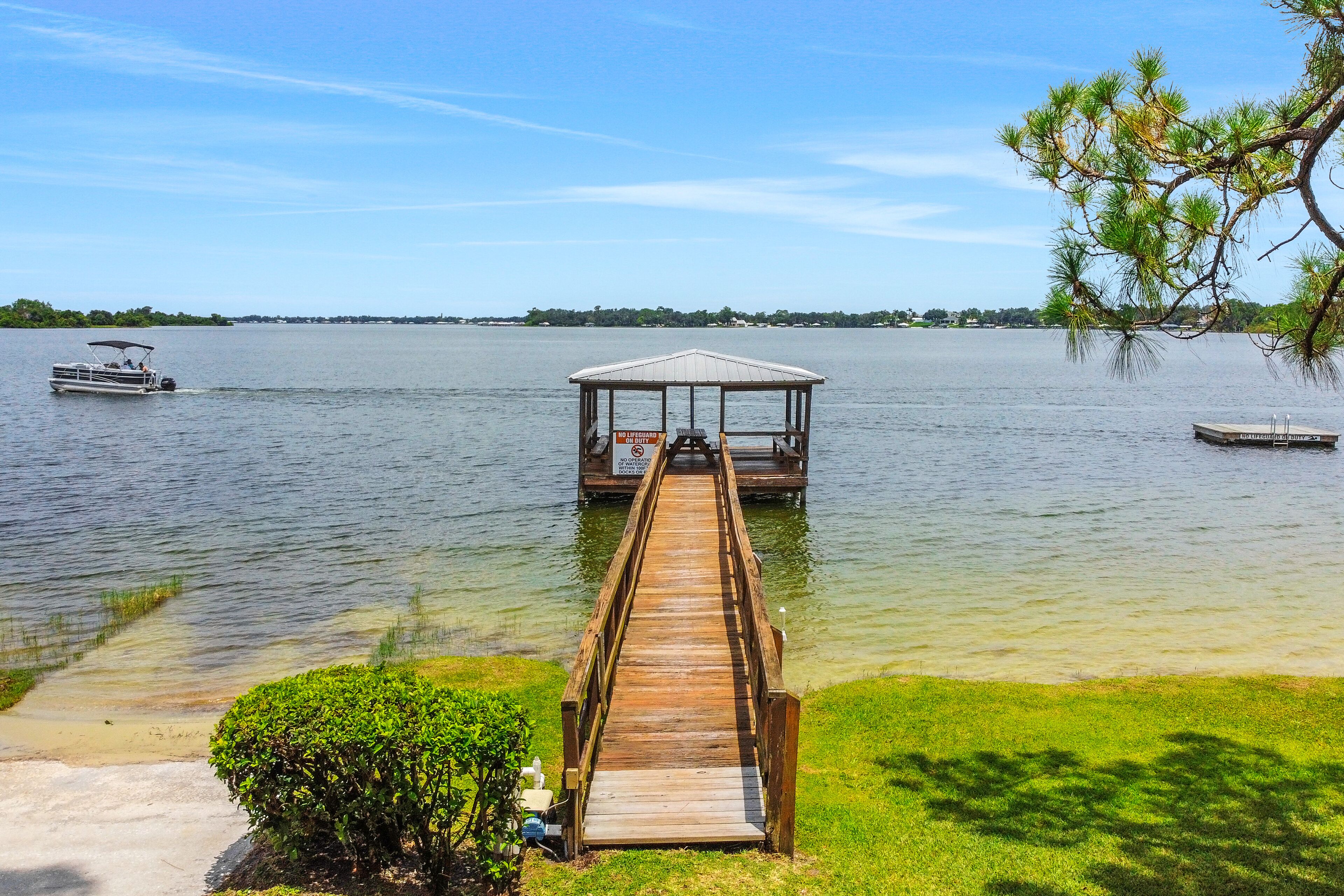 A wooden dock leading to a gazebo over water, surrounded by greenery and clear skies.