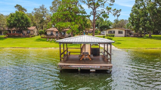 A wooden dock with a covered seating area, surrounded by a grassy area and trees. - Lake June Resort #9 | Condo in Lake Placid (Lake Placid)