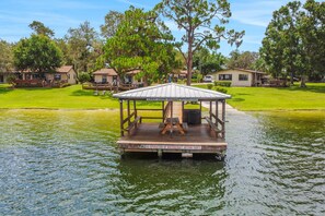 A wooden dock with a covered seating area, surrounded by a grassy area and trees.