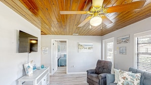 A spacious living area with a wooden ceiling, a grey sofa, a white console table, and a ceiling fan. - Lake June Resort #9 | Condo in Lake Placid (Lake Placid)