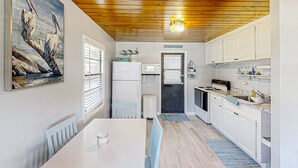 A compact kitchen with white cabinets, a dining table, and a painting of birds on the wall. - Lake June Resort #9 | Condo in Lake Placid (Lake Placid)