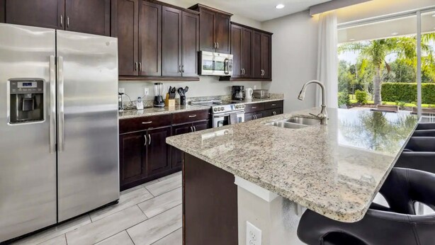 Una cocina moderna con alacenas de madera oscura, electrodomésticos de acero inoxidable, encimeras de granito y una isla grande con taburetes de bar.