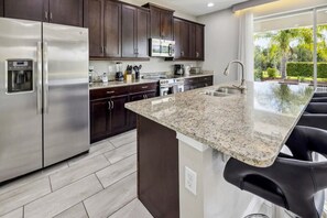 A modern kitchen with dark wood cabinets, stainless steel appliances, granite countertops, and a large island with bar stools. - Encore at Reunion Resort 5BR/5BA near Disney, pool & game room (Kissimmee)