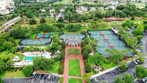 An aerial view of a residential area with a central courtyard, tennis courts, and a swimming pool.