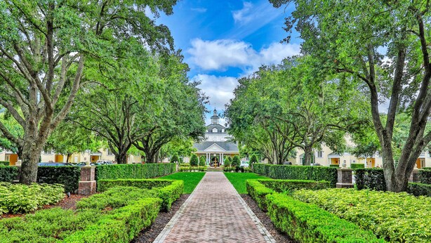 A symmetrical garden pathway leading to a building with a central dome, flanked by neatly trimmed hedges and mature trees.
