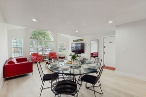 Uma sala de estar moderna com uma mesa de jantar de vidro, cadeiras pretas, um sofá vermelho e uma televisão de tela plana na parede.