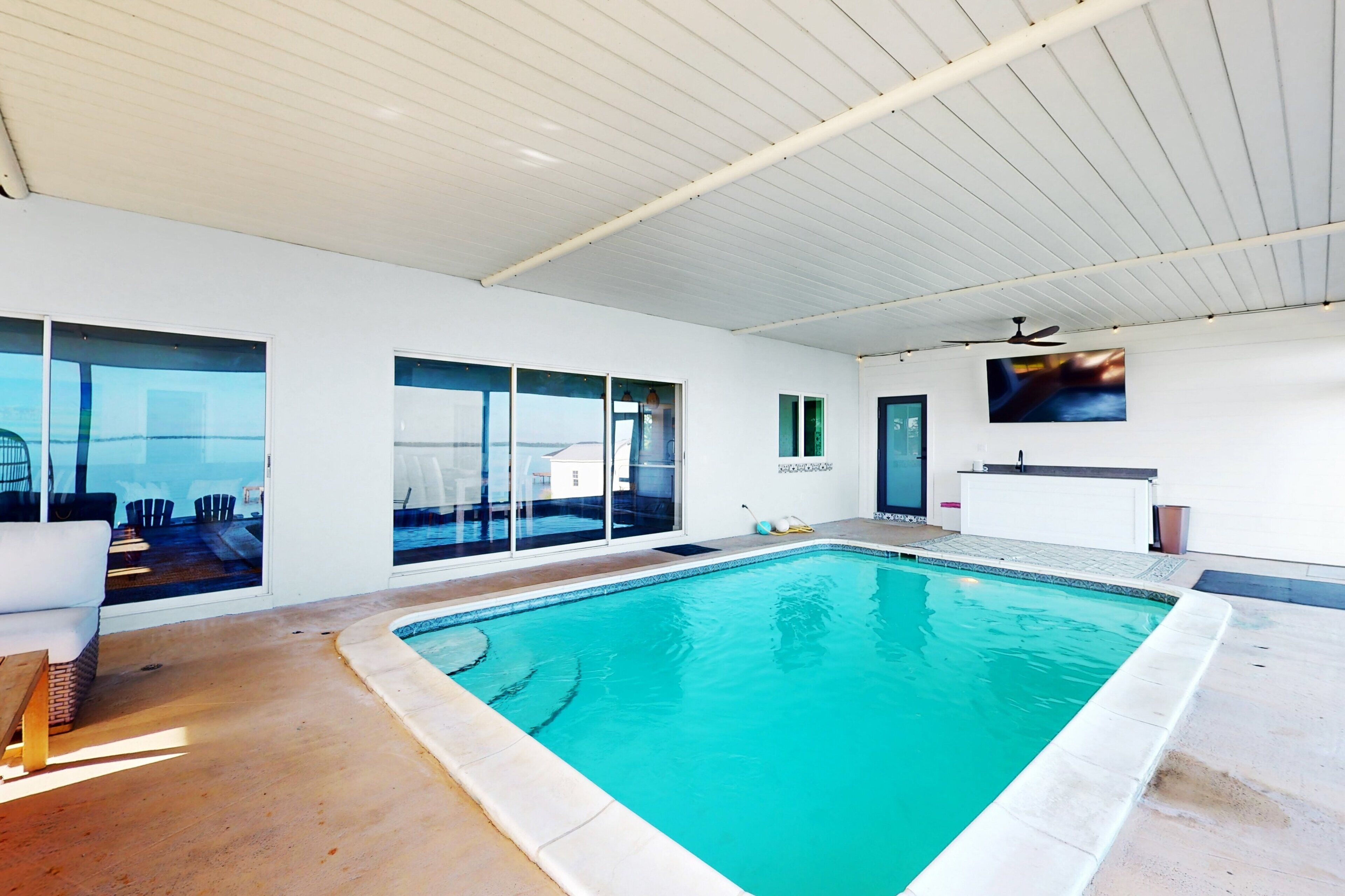 A modern indoor swimming pool with clear glass walls, a ceiling fan, and a view of the cityscape.
