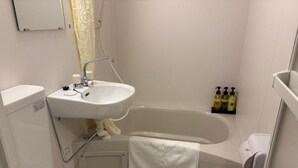 Ein kleines, sauberes Badezimmer mit Waschbecken, Toilette und Badewanne in Weiß. An der Wand befinden sich Pflegeprodukte und ein Handtuch hängt am Badewannenrand.