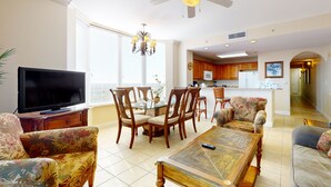 A spacious living room with a flat-screen TV, floral-patterned sofas, a wooden coffee table, and a dining area with a glass-top table and wooden chairs. - Lakefront condo near Disney with lake and city view, pool, hot tub, AC & WiFi (Orlando)