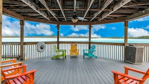 A covered deck with wooden railings, a ceiling fan, and three colorful Adirondack chairs facing a body of water. - Lakefront condo near Disney with lake and city view, pool, hot tub, AC & WiFi (Orlando)
