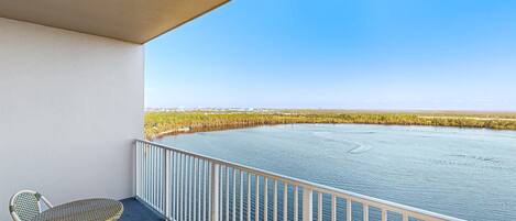 A balcony with wicker chairs and a view of a calm body of water.