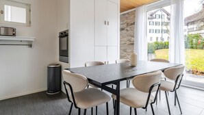 Eine moderne Küche mit Essbereich, mit einem großen Fenster und Blick auf einen Garten sowie Gebäude.