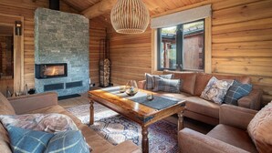 A cozy log cabin interior with a stone fireplace, leather sofas, a wooden coffee table, and a hanging light fixture. - 4 bedroom amazing home in Tuddal (Tuddal)