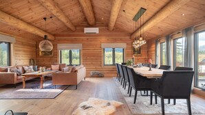 A log cabin interior with a wooden ceiling, a dining area with a long table and chairs, a sofa set, and large windows offering views of the outdoors. - 4 bedroom amazing home in Tuddal (Tuddal)