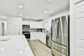 A modern kitchen with white cabinetry, stainless steel appliances, and a marble countertop.