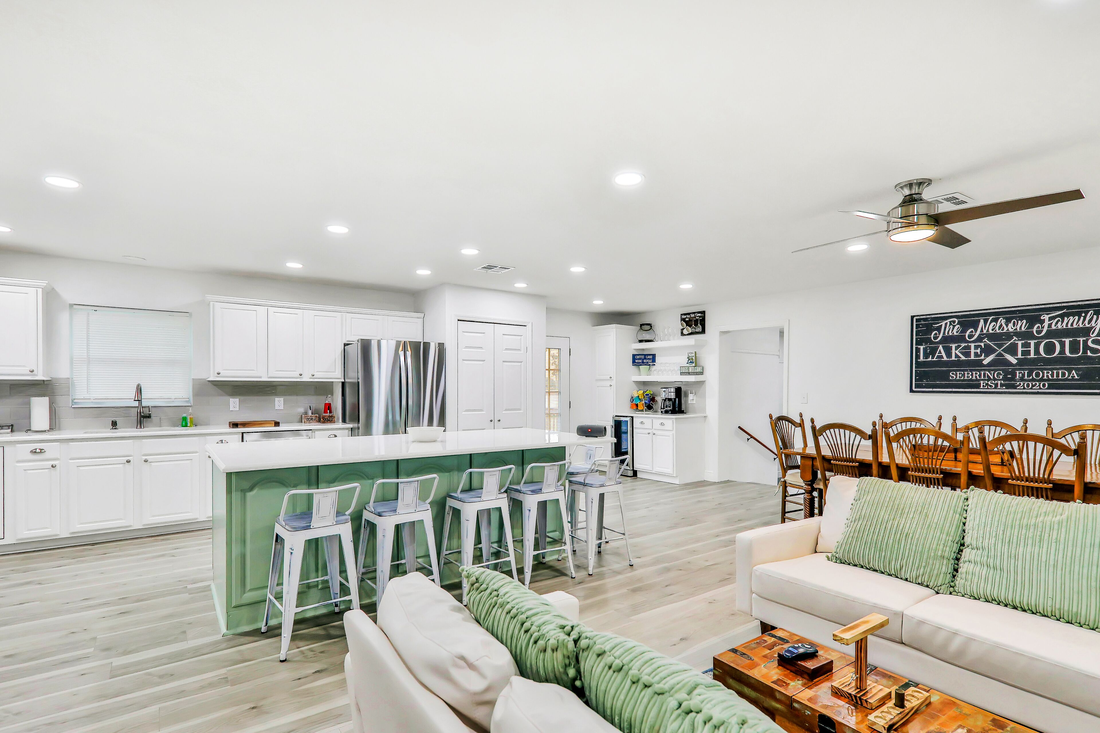 A modern kitchen with white cabinets, a stainless steel refrigerator, and a bar area with stools.