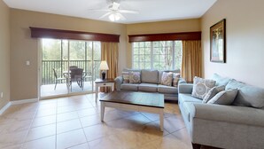 Ein geräumiges Wohnzimmer mit Deckenventilator, einer Couch, einem Couchtisch und einem Essbereich mit Stühlen und einer Lampe.